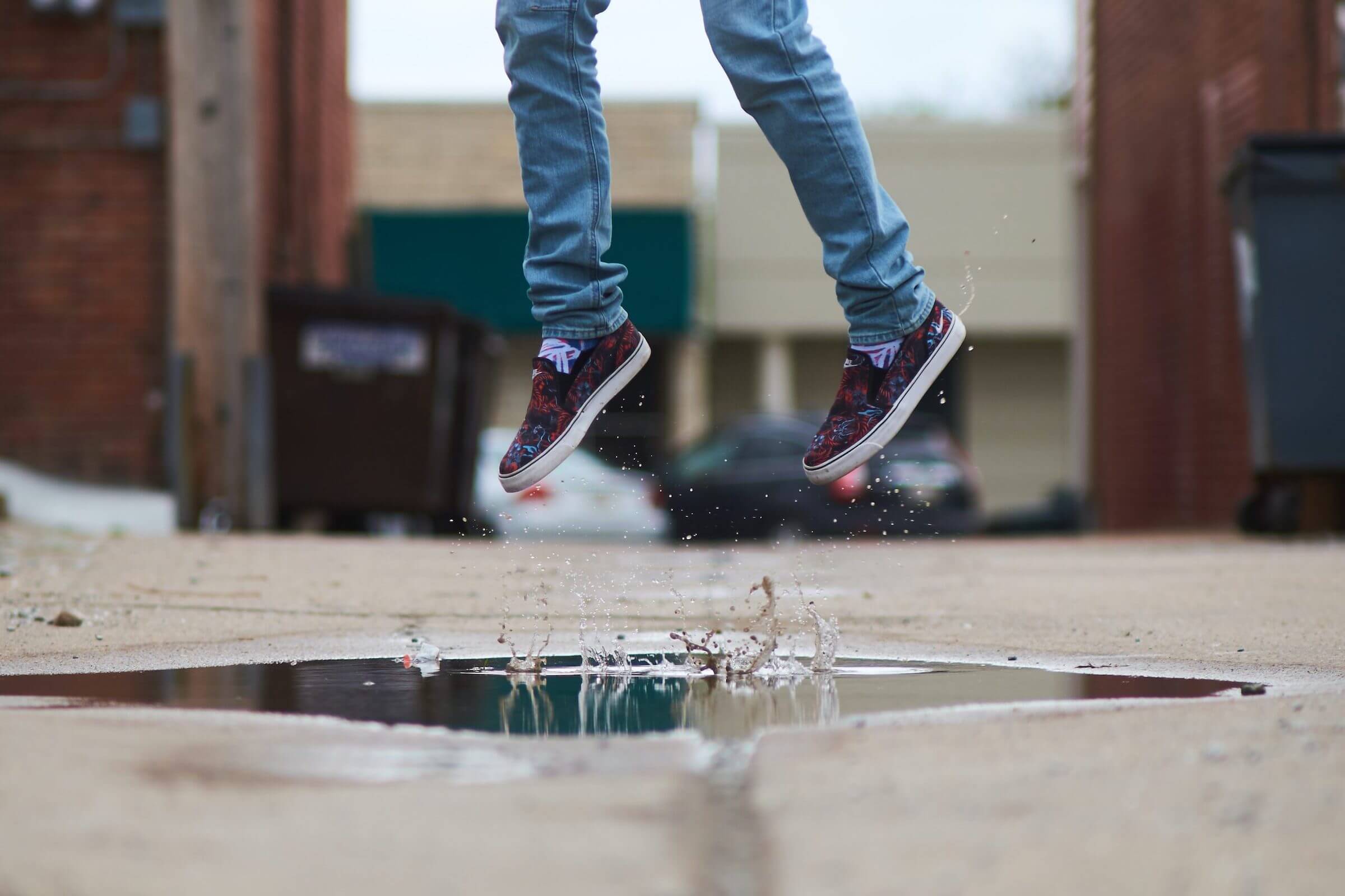 person wearing jeans jumping high in a puddle having fun